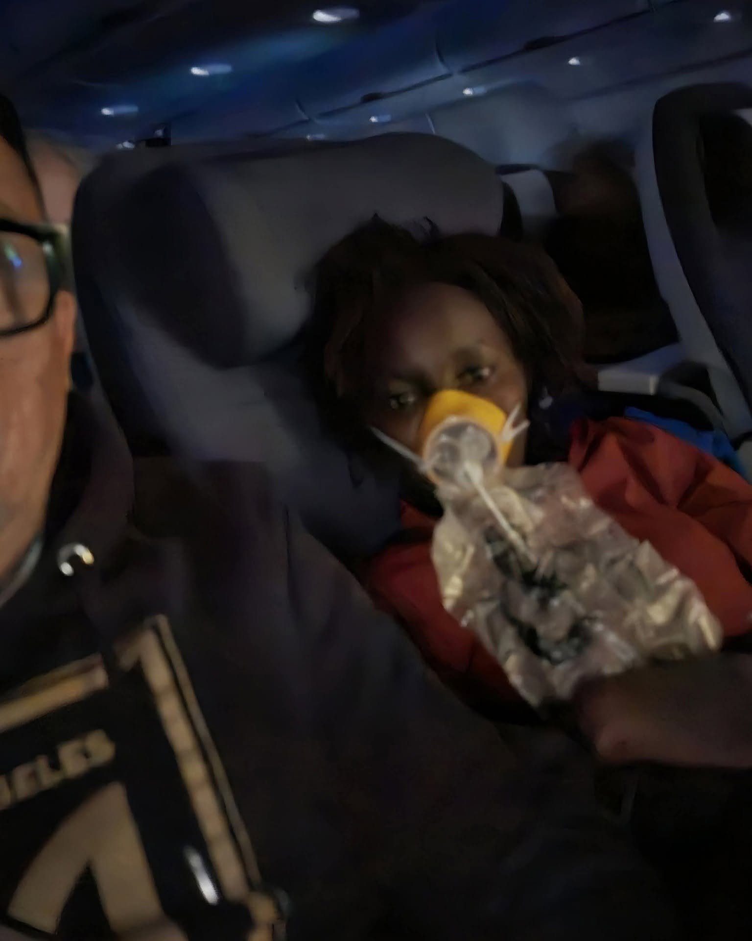 : Linda Chebet Gomez flight medical emergency showing her wearing an oxygen mask on an airplane seat next to her husband.