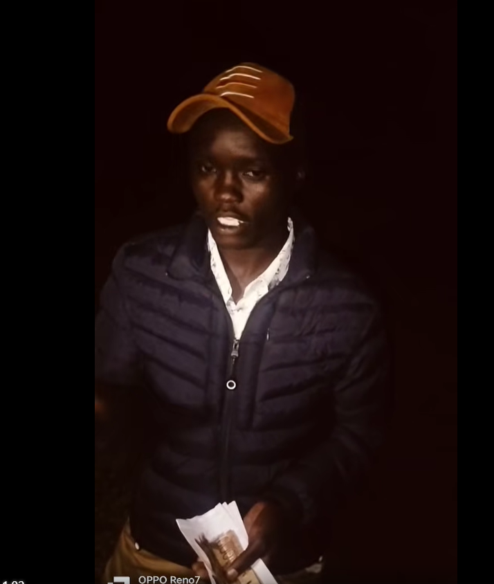 Man in a tan cap and navy puffer jacket holding recovered cash after a burial fundraiser theft in Elgeyo Marakwet.