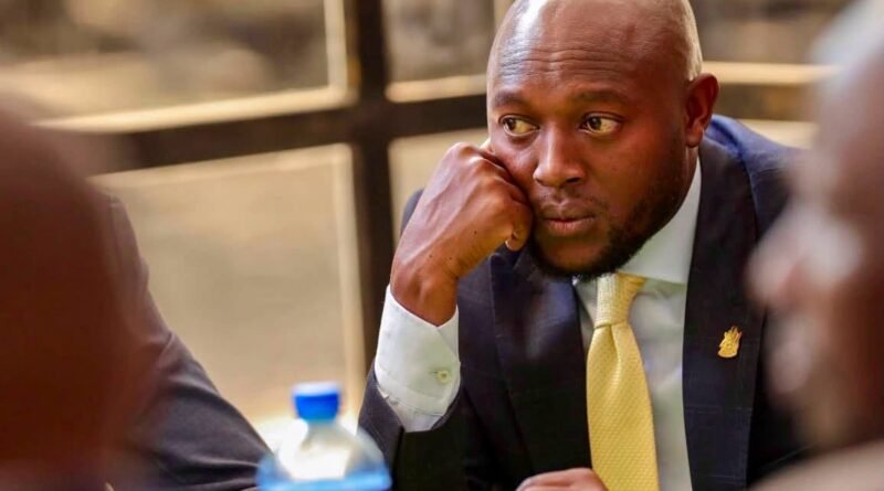 Stephen Letoo resting his chin on his right hand with a pensive expression during a formal meeting.