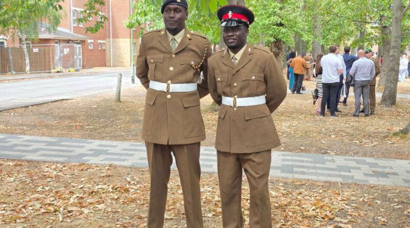 Two Kenyan British Army soldiers, Nahashon Kipkosgei Rutto and Titus Kiplagat, wearing formal brown service dress uniforms and white ceremonial belts outdoors after their graduation.
