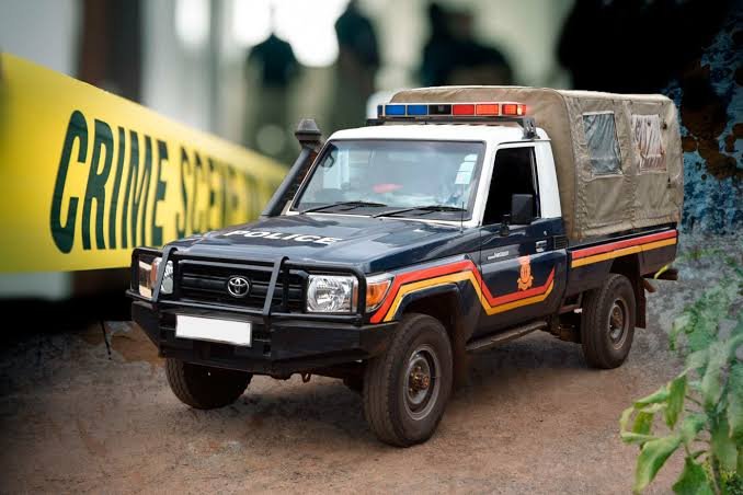 A dark-colored police pickup truck with a snorkel and covered cargo bed is parked on dirt ground next to a large yellow "CRIME SCENE" banner.