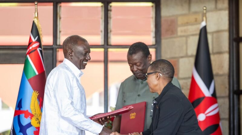 President William Ruto holds a red document folder while shaking hands with a woman at Eldoret State Lodge, with Kenyan flags in the background