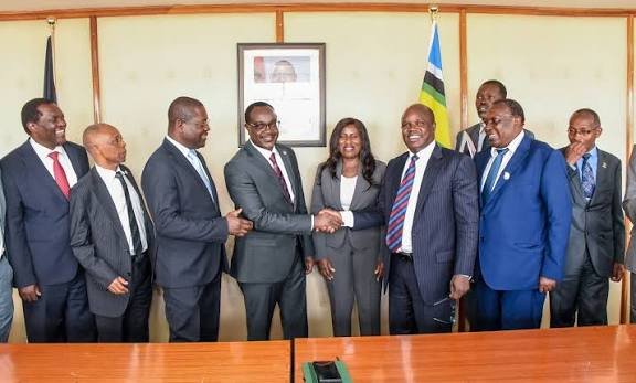 Group of officials in suits standing together during an indoor meeting, with two men shaking hands